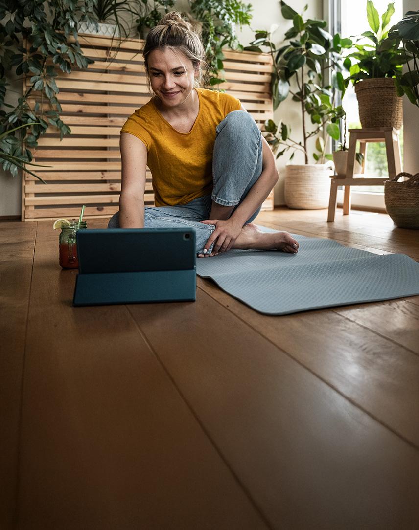 Lächelnde Frau auf Yogamatte schaut auf ihr Tablet