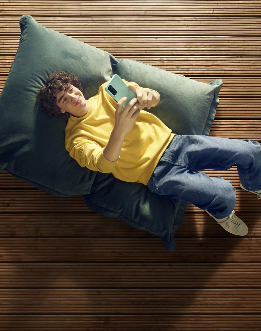 Jugendlicher Junge in gelbem Pulli macht liegend ein Selfie von sich